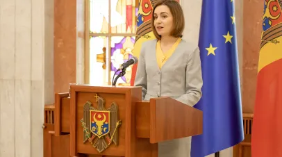Moldovan President Maia Sandu stands at a podium with Moldovan flags behind her