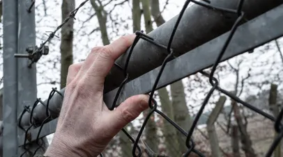 Hand climbing a containment fence with barbed wire