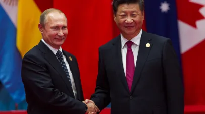 Russian President Putin and Chinese President Xi Jinping shake hands in front of row of flags