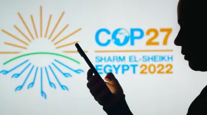  a woman's silhouette holds a smartphone in front COP27 logo 