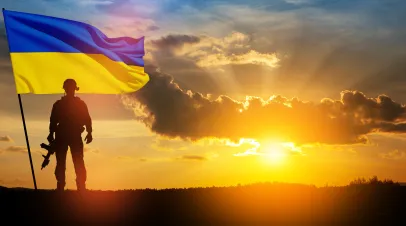 Flag of Ukraine with silhouette of soldier against the sunrise or sunset.