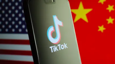 TikTok app logo on a smartphone screen and flags of China and United States on the blurred background.