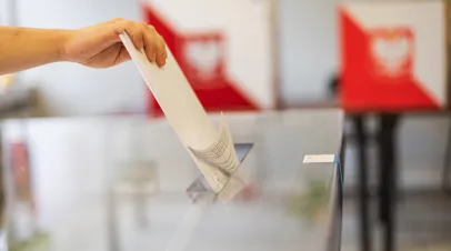 Throwing a card with a vote to the ballot box during elections. In the backround polish arms and flag