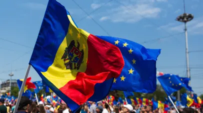 A crowd of people with one person holding up the flags of Moldova and the European Union on flag poles. 