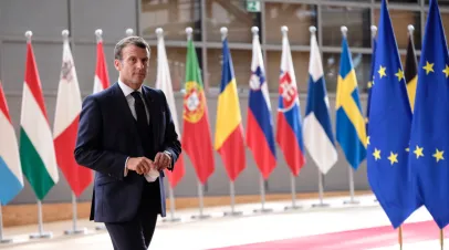 French president Macron walking in front of a line of EU member flags