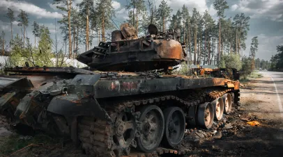 A destroyed Russian tank with burned forest behind it