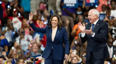 Picture of Vice President Kamala Harris and Governor Tim Walz at a rally waving from the stage