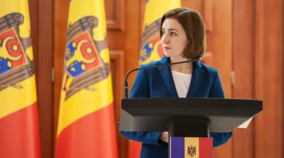 Moldovan President Maia Sandu satanding at a podium in front of several Moldovan flags