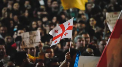 Person in a large crowd of protestors waving a Georgian flag