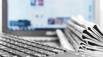 A stack of newspapers in front of a computer screen and keyboard