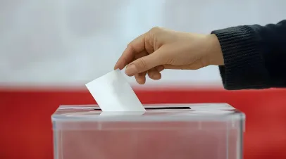 Hand putting a ballot in a box before a polish flag