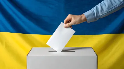 Hand reaching out to put a ballot in a box in front of a Ukrainian flag