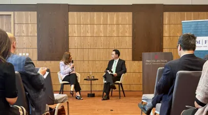 Two people sitting at the head of a room speaking into microphones