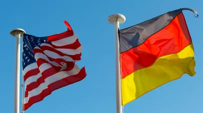 Two National Flags of both United States of America and Germany waves against clear blue sky background