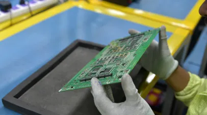 A quality control technician carefully examining a printed circuit board (PCB) populated with surface-mounted electronic components after the SMT (Surface Mount Technology) assembly process. 