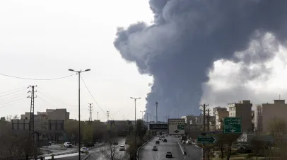 Cars drive down a highway as smoke billows after overnight airstrikes on oil depots on March 8, 2026 in Tehran, Iran.