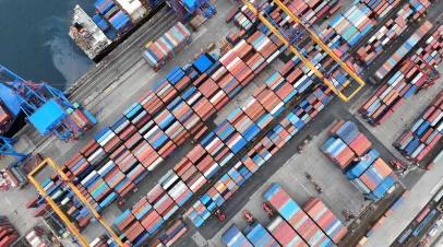 Overhead view showing cargo container vessel navigating maritime shipping route, loading international freight in busy industrial harbor