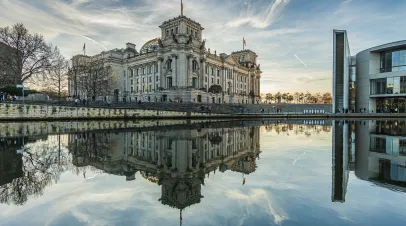 historic Reichstag building in Berlin during the day in winter. River Spree with reflection from the building in the government district. Sunshine in the background with cloudy skies.