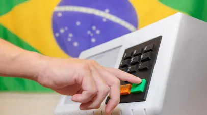 Brazilian electronic ballot box during presidential elections, with a voter pressing the confirm button. Concept of democracy, civic duty, and electoral process in Brazil. In the background, the Brazilian flag.