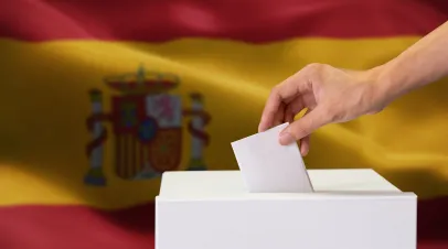 Close-up of human hand casting and inserting a vote and choosing and making a decision what he wants in polling box with Spain flag blended in background