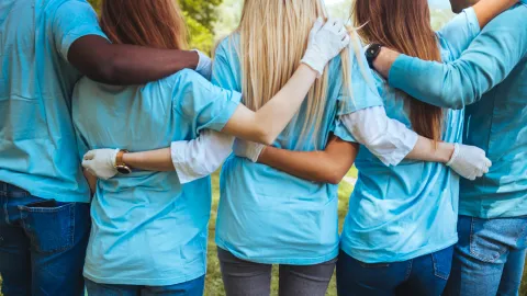 Volunteering, people and ecology concept. Group of volunteers embracing in park, back view, copy space