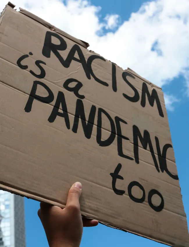 Protestor holds a "Racism is a pandemic too" sign at a Black Lives Matter protest on Alexanderplatz Berlin.