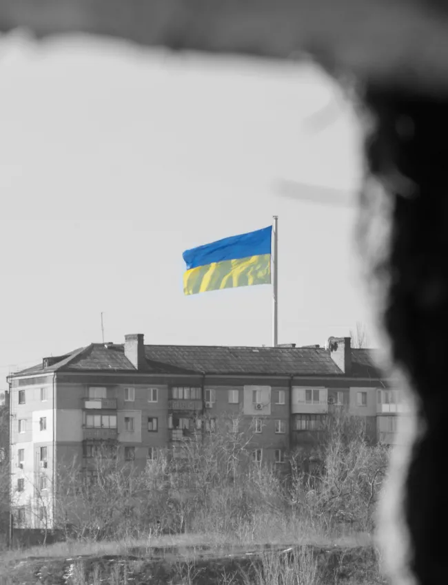 View through the window of the ruined house on the flag of Ukraine in the blue sky.