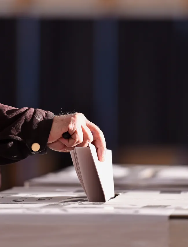 Hand of a person casting a vote into the ballot box during elections