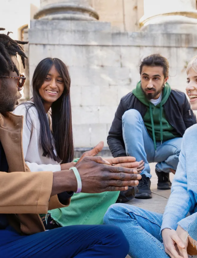 Group of diverse young adults engaging in lively conversation on university grounds. Represents multicultural friendship, inclusivity, and community in higher education settings.