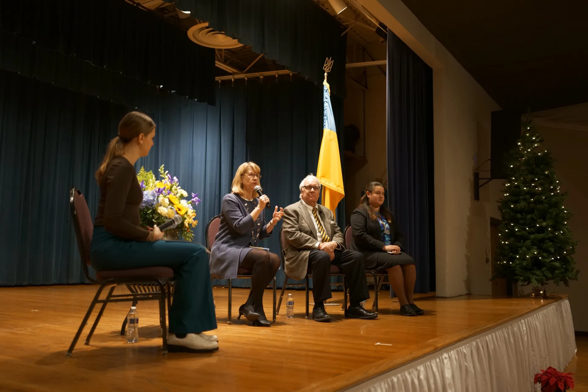 Four people on a stage speaking with a Ukrainian flag on a pole behind them